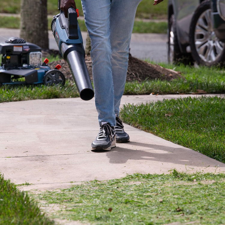 Person walking with a leaf blower on a sidewalk