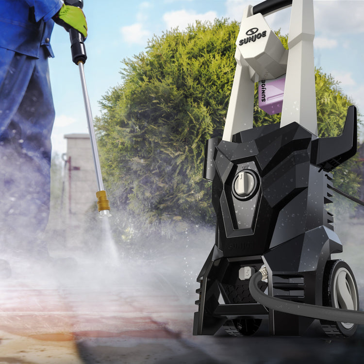 Person using a pressure washer to clean a driveway with a tree in the background