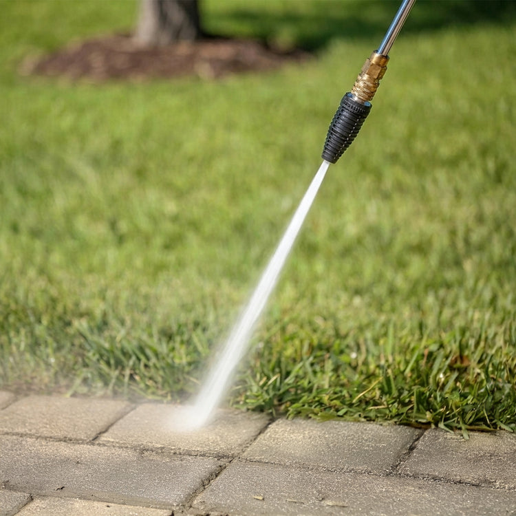 Pressure washer nozzle spraying water onto a concrete surface with grass in the background