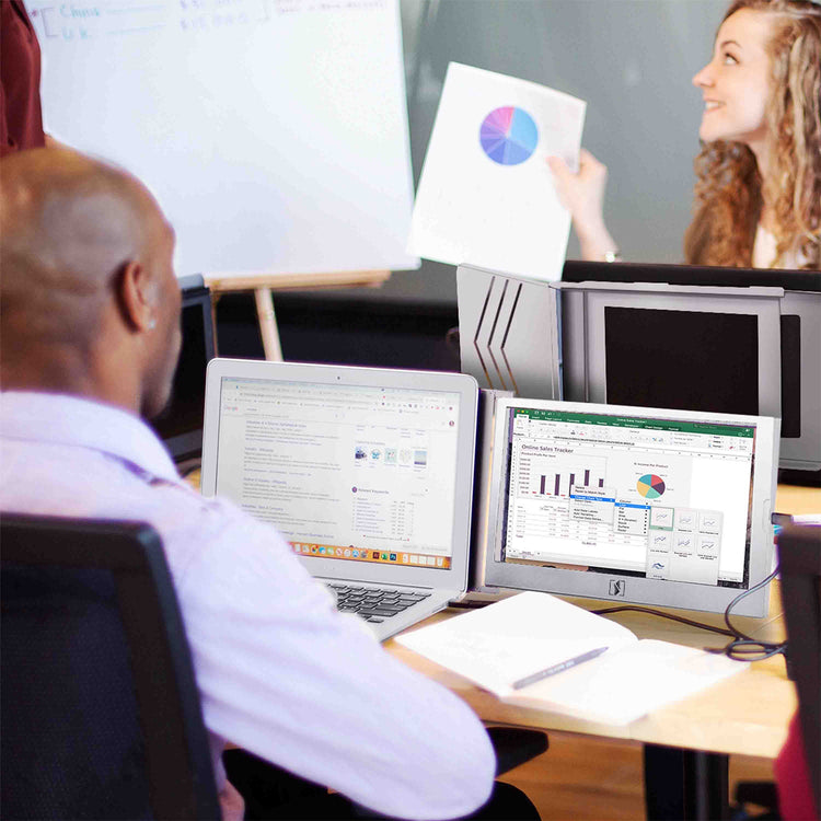 Two people working at a desk with computers and a whiteboard in the background