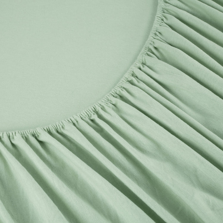 Close-up of a green fitted sheet with a soft texture on a light green background.