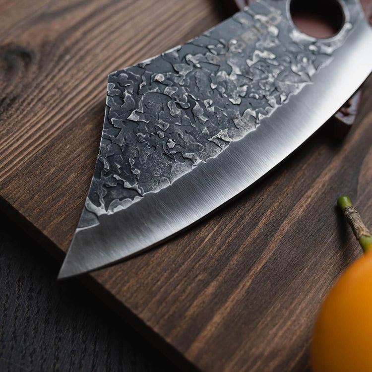 Close-up of a large knife with a textured blade on a wooden surface