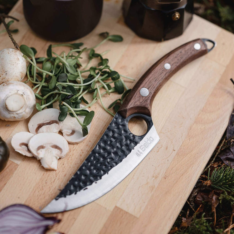 Wooden cutting board with sliced mushrooms, fresh greens, and a knife with a wooden handle.