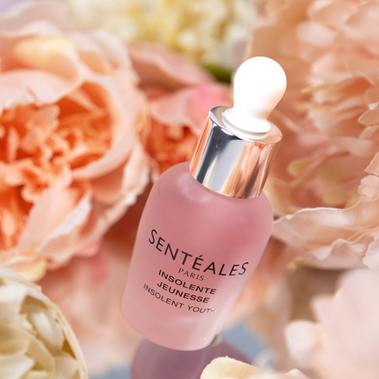 Pink skincare bottle with dropper labeled 'Senteéales' surrounded by flowers