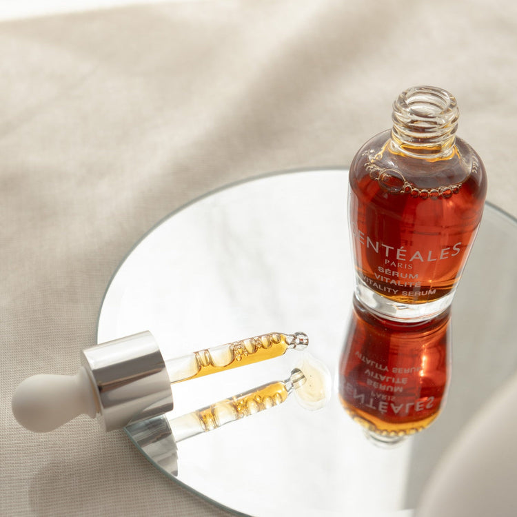 Bottle and dropper of a skincare serum on a reflective surface with a neutral background