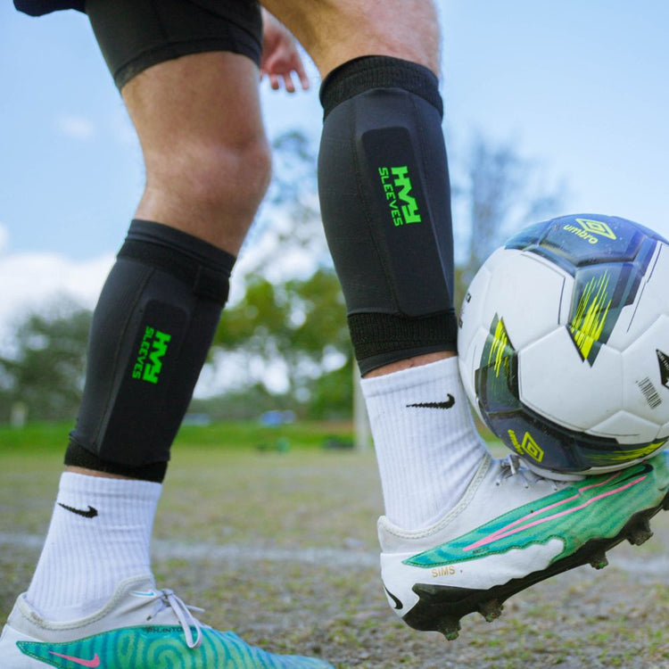 Person wearing shin guards and soccer cleats with a soccer ball on a grass field.