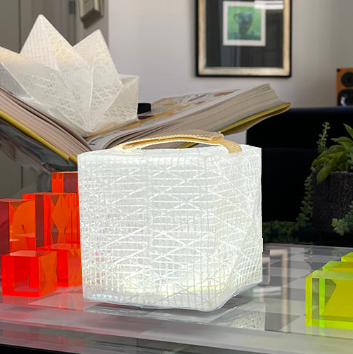Modern cube-shaped lamp on a table with books and colorful objects in the background