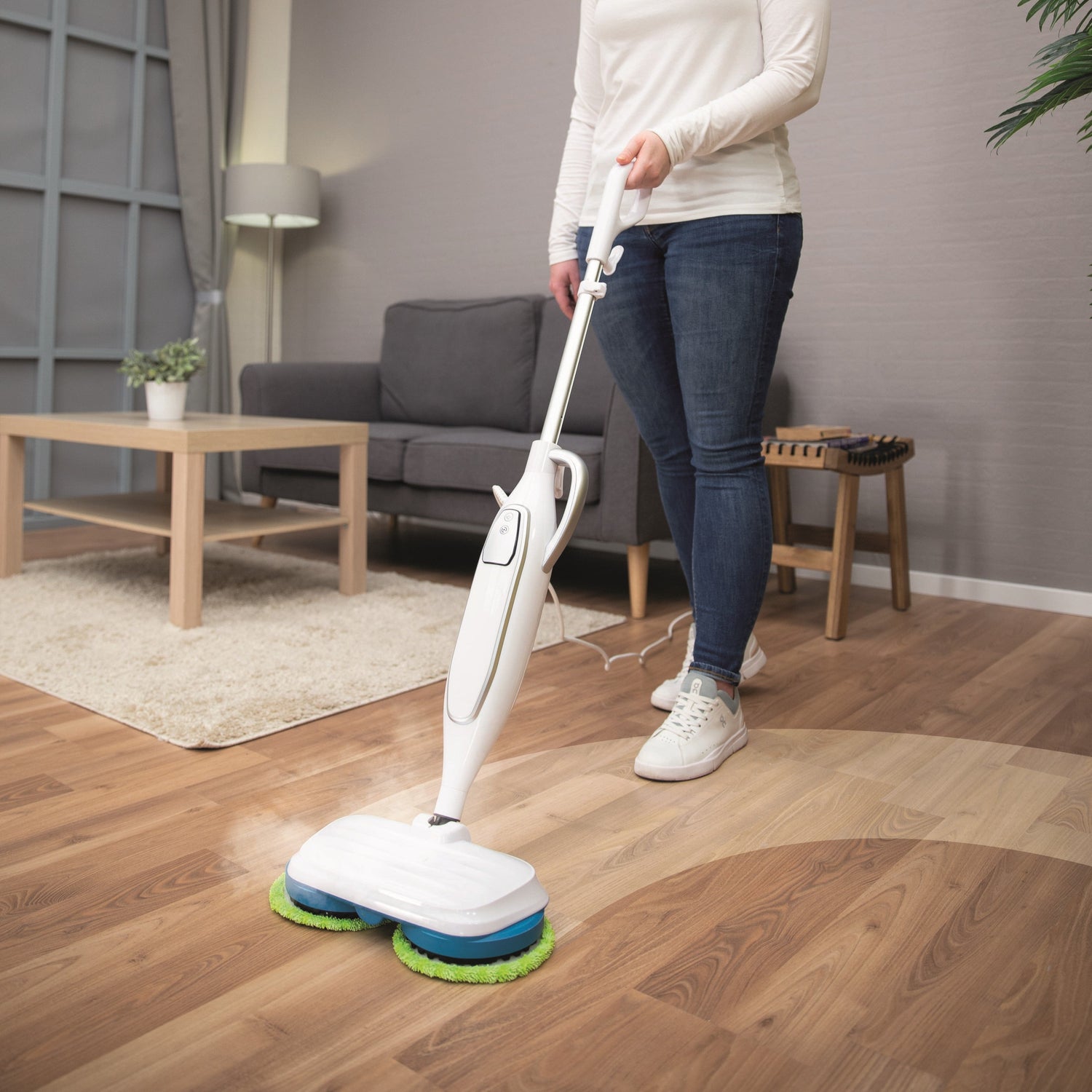 Person using a floor cleaning device on a wooden floor in a living room.
