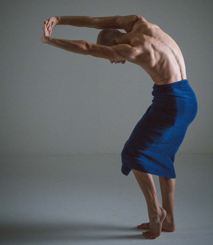 Man in a blue towel performing a yoga pose against a gray background