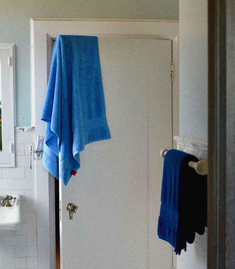 Bathroom with a blue towel hanging on a door and another on a rack.