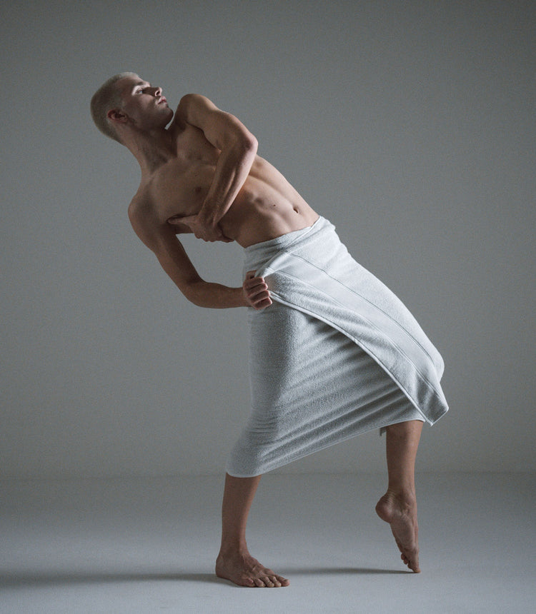 Man in a towel performing a yoga pose against a plain background