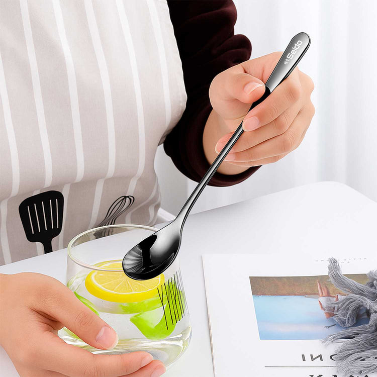 Person holding a glass with lemon slices and a spoon, with a white background