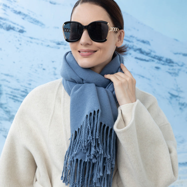 Woman wearing a blue scarf and sunglasses against a light blue background