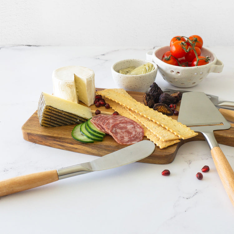 Wooden charcuterie board with cheese, salami, crackers, and a knife on a white surface.