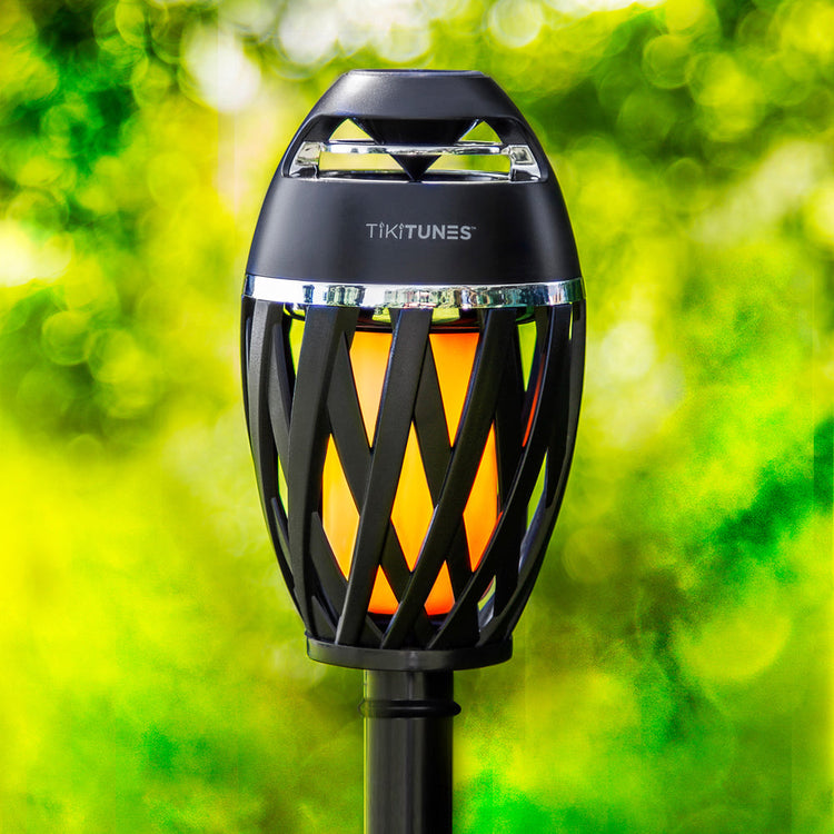 Tiki torch with built-in speaker labeled 'TIKITUNES' against a green foliage background