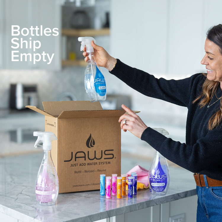Woman opening a JAWS product box with bottles on a kitchen counter.