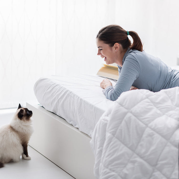 Woman lying on a bed with a cat next to her, both looking at a book.
