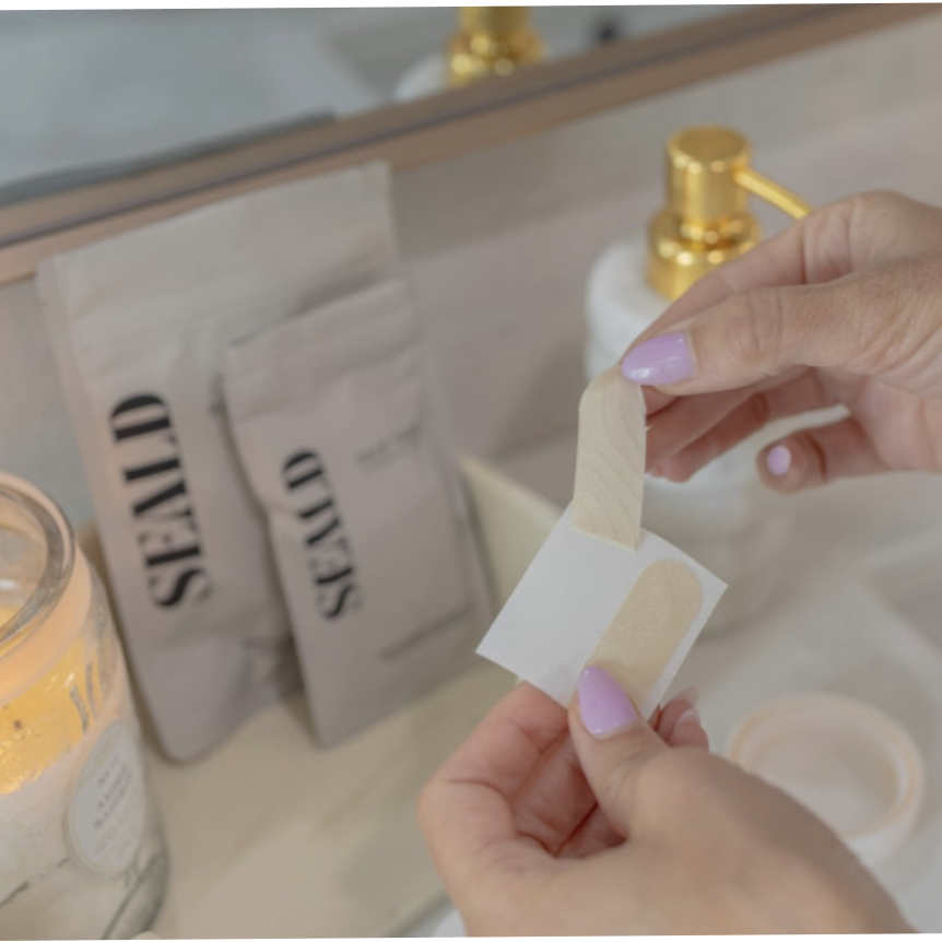 Person holding a seald face tape over a sink with a candle and seald packaging in the background