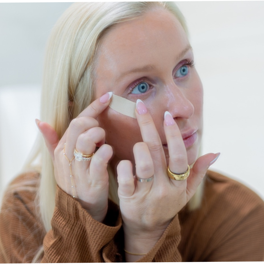 Woman applying a seald face tape to her face with a white background