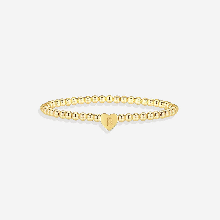 Gold beaded bracelet with a heart-shaped tag on a white background