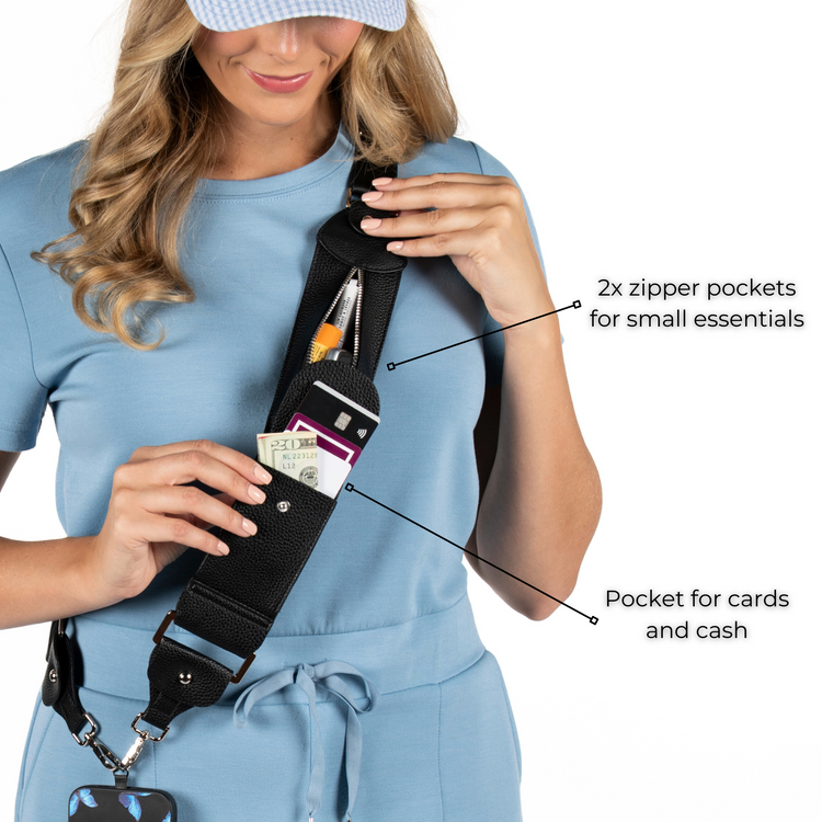 A person wearing a blue shirt is using a black crossbody accessory called Stashie to hold a phone case. The Stashie has an adjustable strap and multiple pockets, including two zipper pockets and a pocket for cards and cash.
