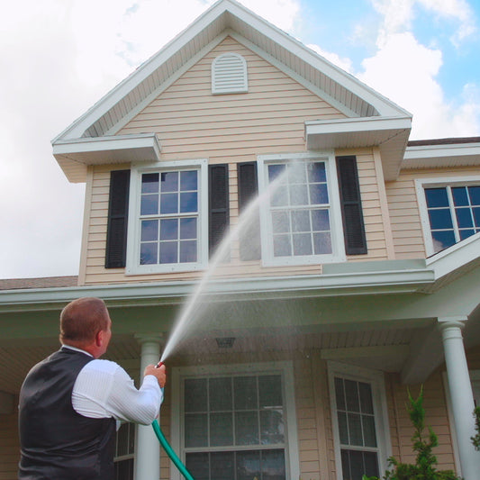 A person using a hose to spray a window cleaning solution on a house window.