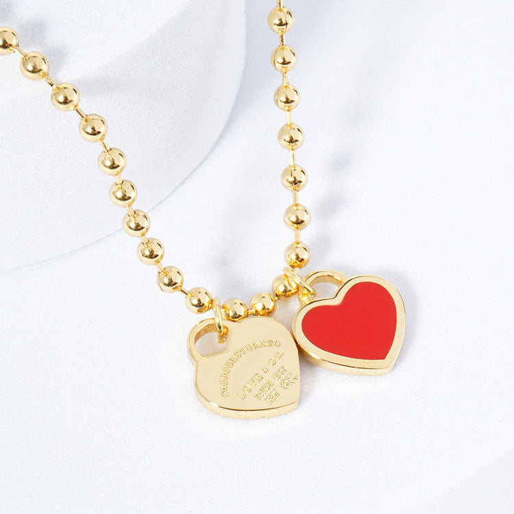 A gold-colored necklace featuring a ball chain design with two heart-shaped pendants.