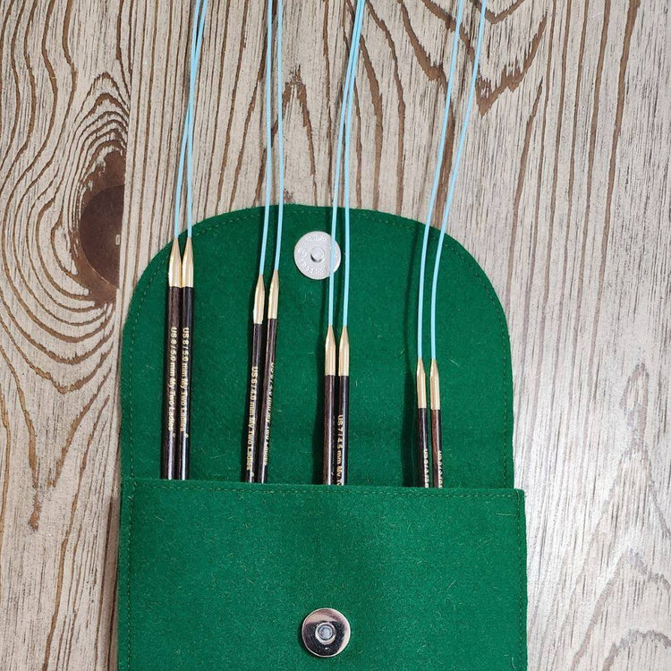 Set of knitting needles in a green case on a wooden surface