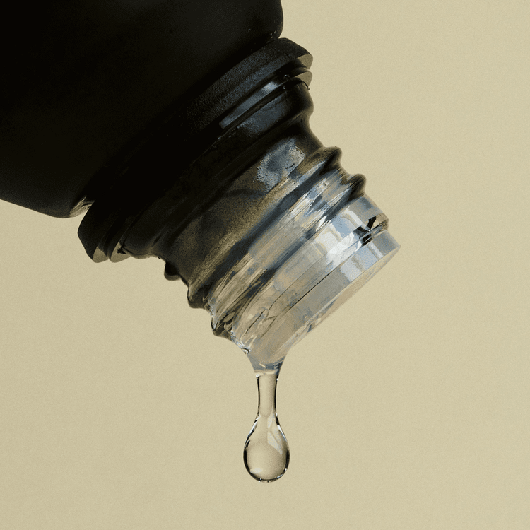Close-up of a dropper bottle with liquid dripping against a beige background