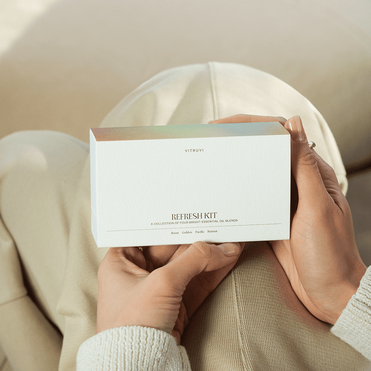 Person holding a white box labeled 'NATRUE' with 'REFRESHKIT' on a neutral background
