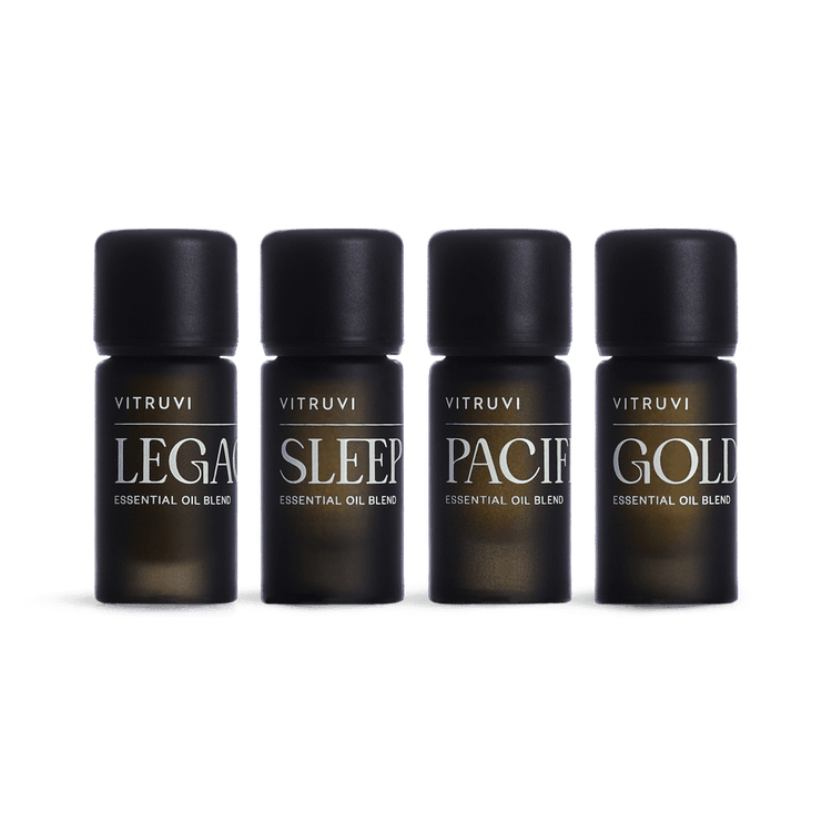 Four Vitruvi essential oil bottles labeled 'Legacy', 'Sleep', 'Pacify', and 'Gold' on a green background.