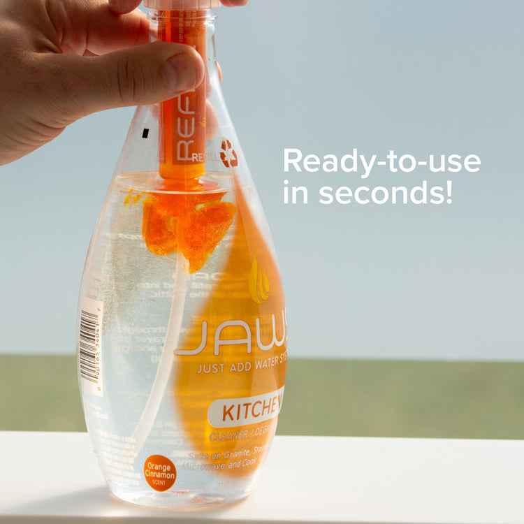 Bottle of JAW kitchen cleaner with a hand holding the spray nozzle against a light background.