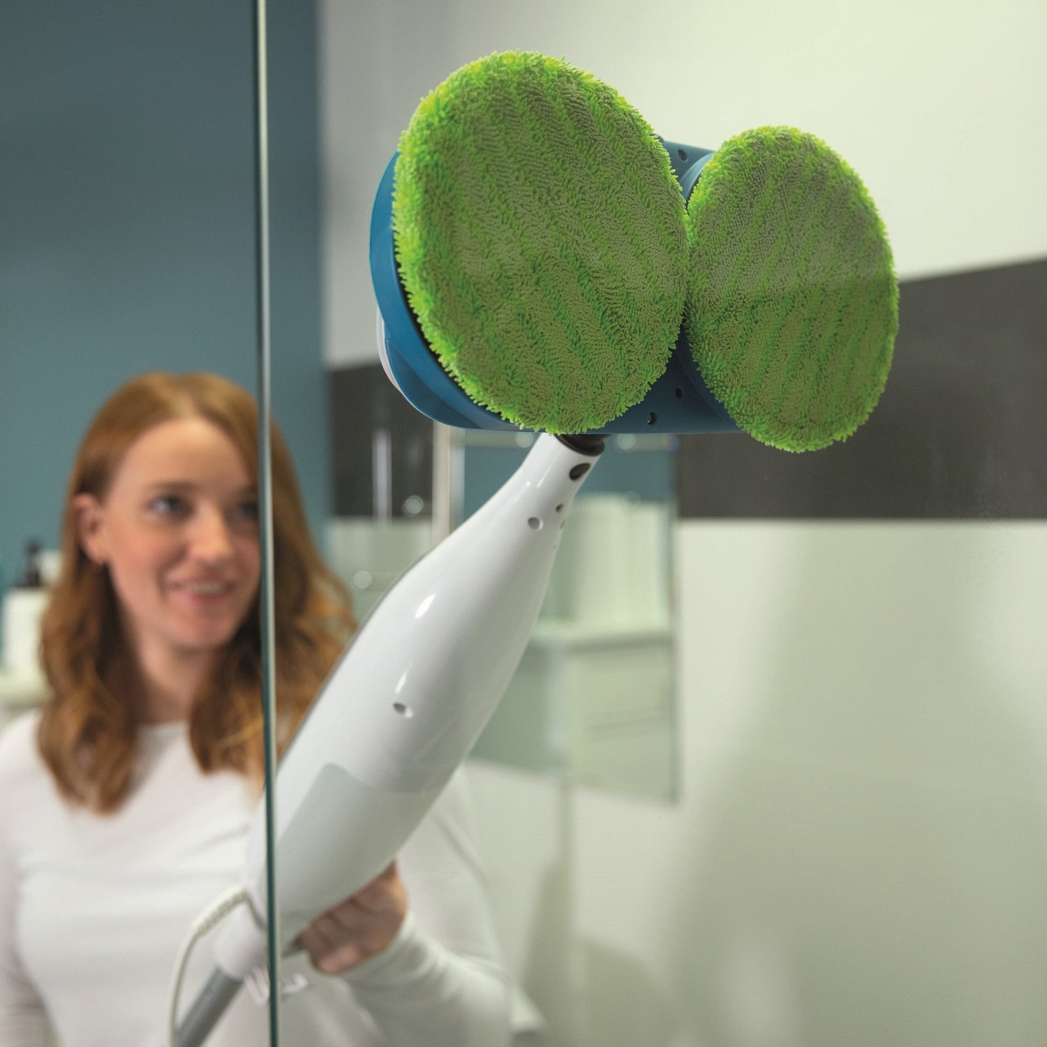 Person using a cleaning tool with green pads to clean a glass surface.