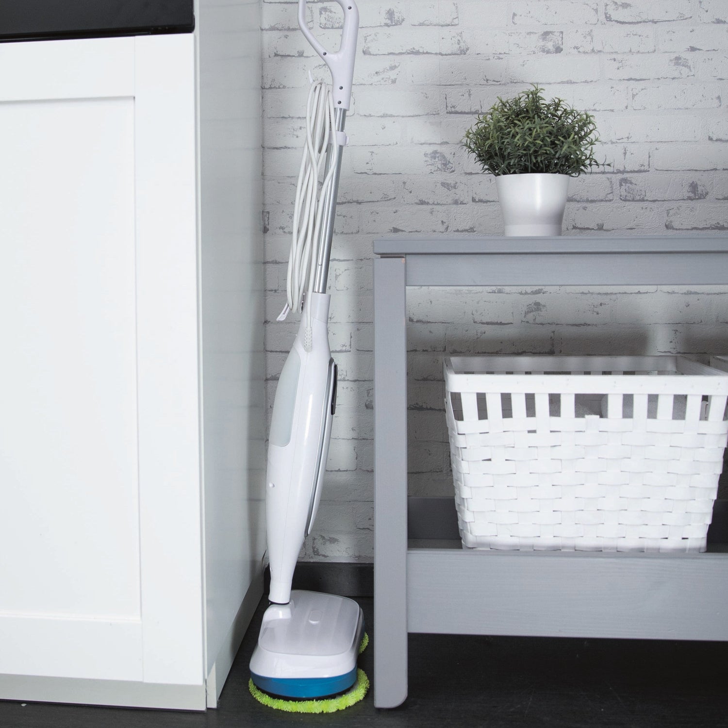 White vacuum cleaner with green brush head on a black floor next to a white cabinet and gray table.