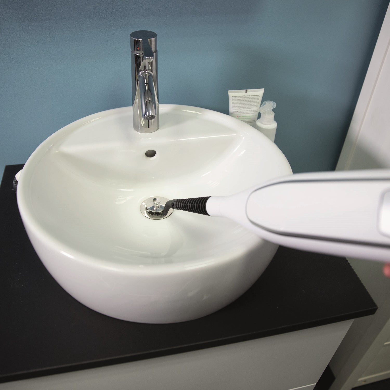 White sink with a black and white device being used on it, against a blue wall.