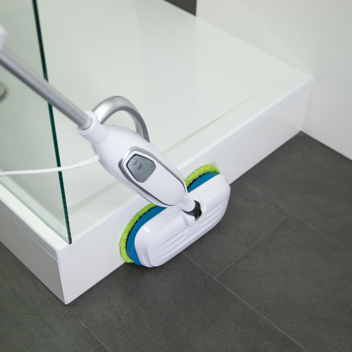 Cleaning tool with a white handle and green and blue base cleaning a tiled floor.