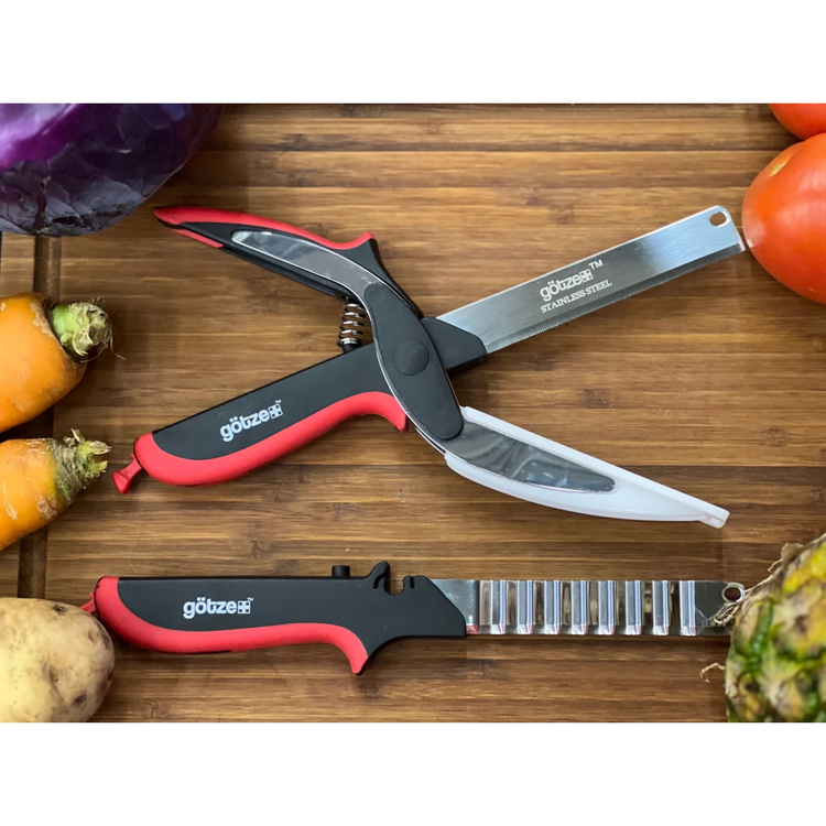 A pair of Gotze kitchen shears with red and black handles laid on a wooden surface surrounded by various fruits and vegetables.