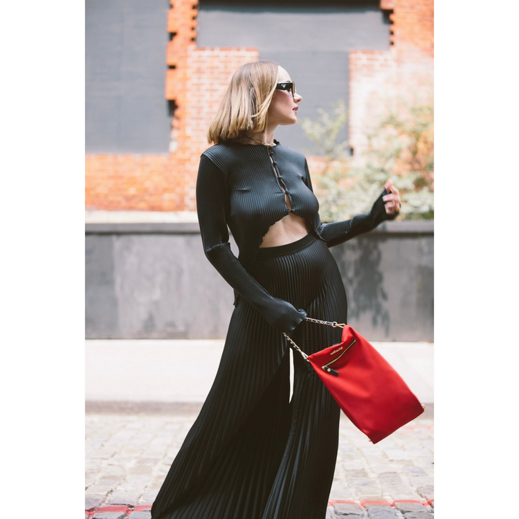 Woman in a black outfit with a red bag standing outdoors.