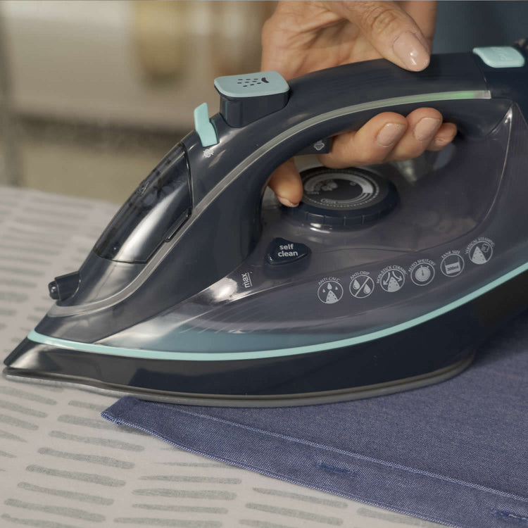 Person ironing fabric with a modern steam iron on a table.