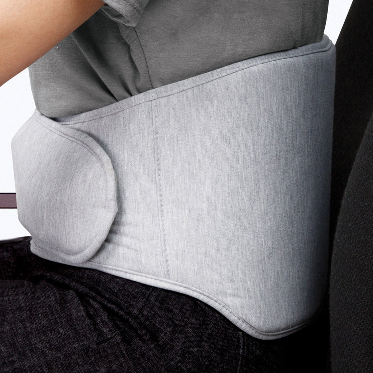A person seated with a gray back wrap around their lower back, featuring inflatable lumbar support and adjustable straps.