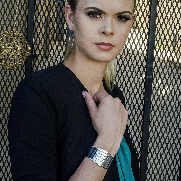 A person wearing a black top and a silver-colored cuff bracelet with an engraved serenity prayer on it.