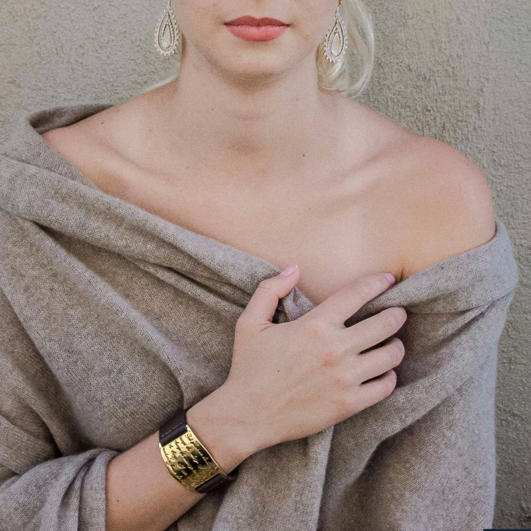 A person with a light complexion wearing a beige knit sweater and a gold-plated cuff bracelet with a serenity prayer inscription.