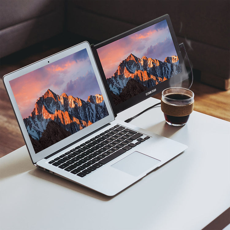 Two laptops displaying mountain scenery on a table with a steaming cup of coffee.
