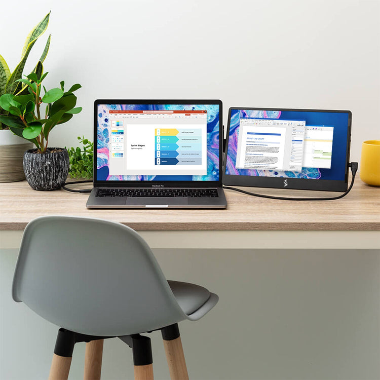 Laptop and monitor on a desk with a plant and chair in the background