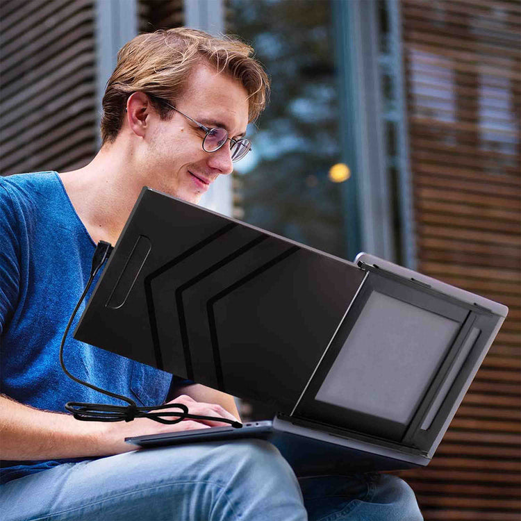 Person using a laptop with an additional screen attached outdoors.