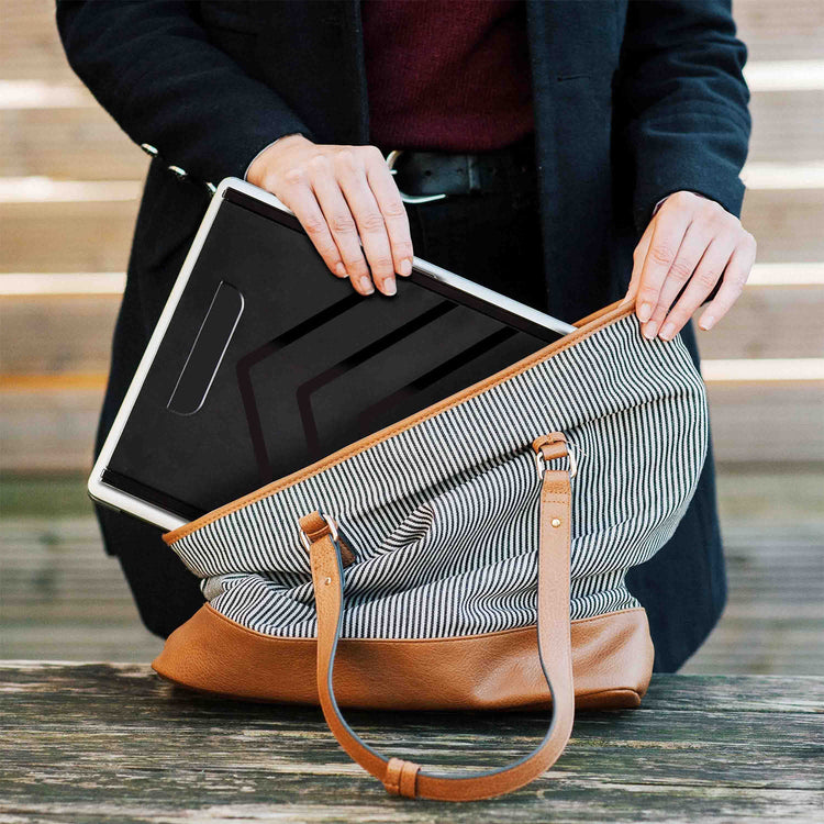 Person holding a black laptop in a striped bag with a brown strap.