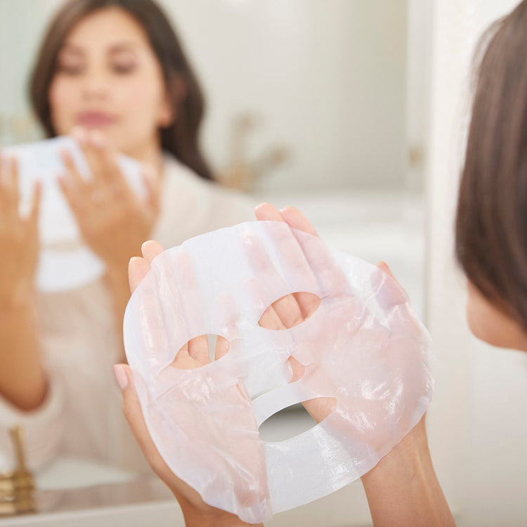 Person holding a sheet mask in front of a mirror