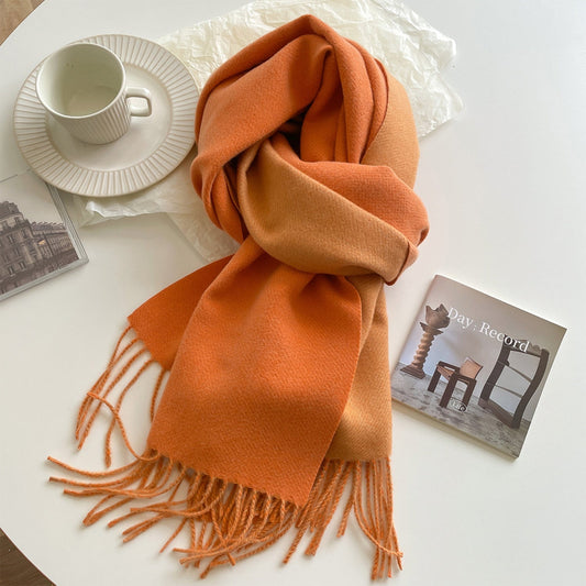 A green reversible pashmina scarf with fringe detailing, displayed on a white surface next to a beige coat and a pretzel.