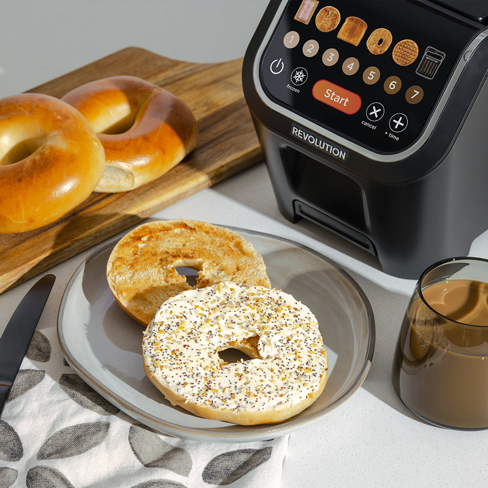 Bagels on a plate with a bagel machine and coffee in the background