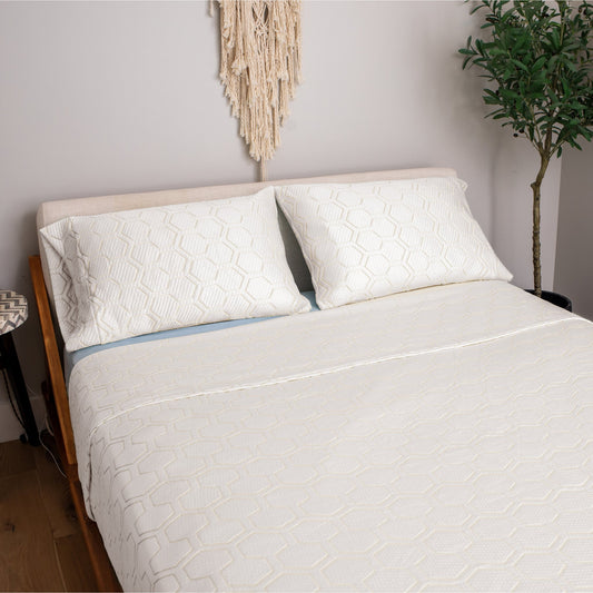 Bed with white textured bedding and pillows in a bedroom setting.